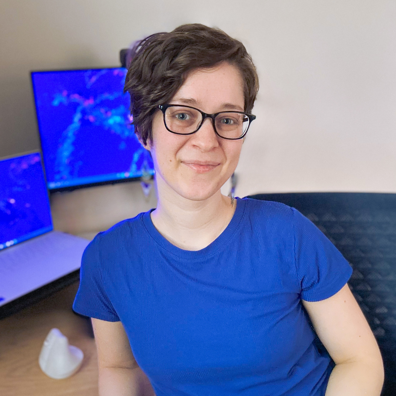 Ariel M. Lighty: woman with short wavy pixie haircut wearing glasses and a blue shirt.